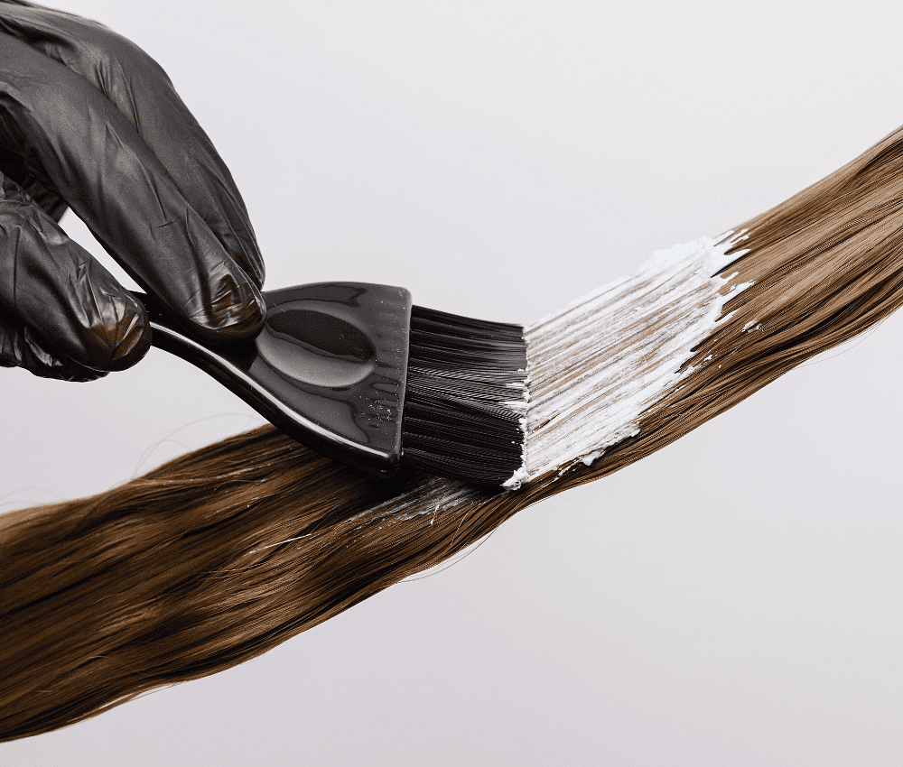 Brush applying dye on a strand of brown hair.